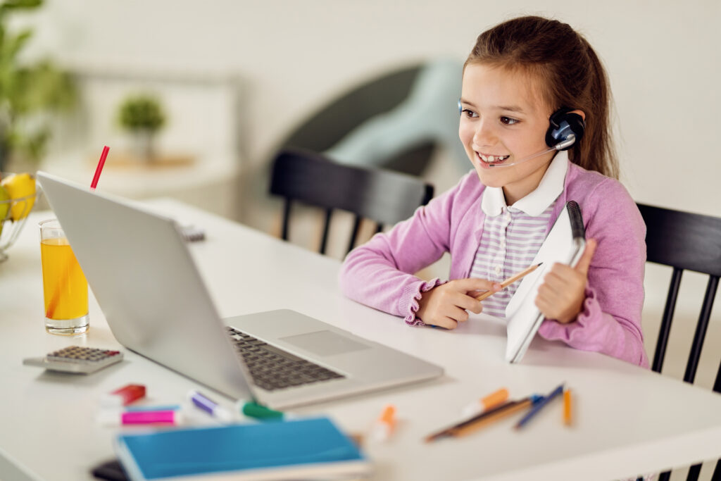 Happy girl using computer and talking to her teacher via video call while learning at home. Online learning
